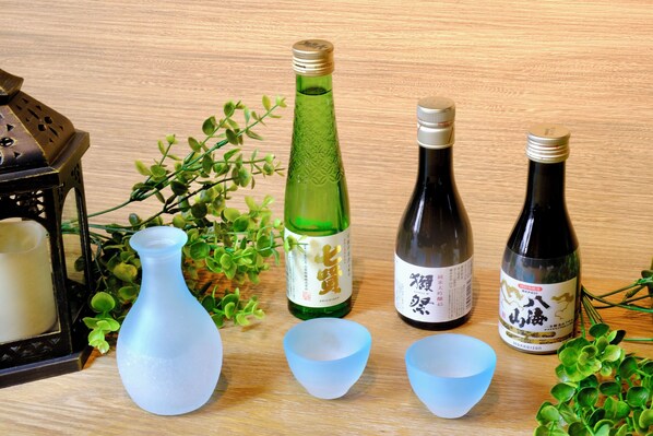 A wooden table with various items including a green bottle, two dark bottles, a white candle, and a blue vase.
