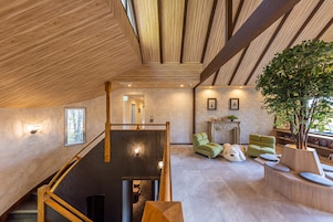 Un interior espacioso con techo de madera, una escalera, una chimenea y un gran árbol.