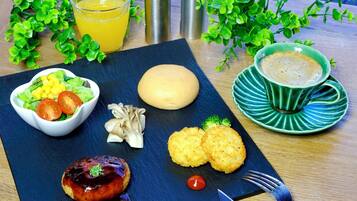 A meal with a salad, grilled meat, and bread on a slate board, accompanied by a cup of coffee and a glass of orange juice.