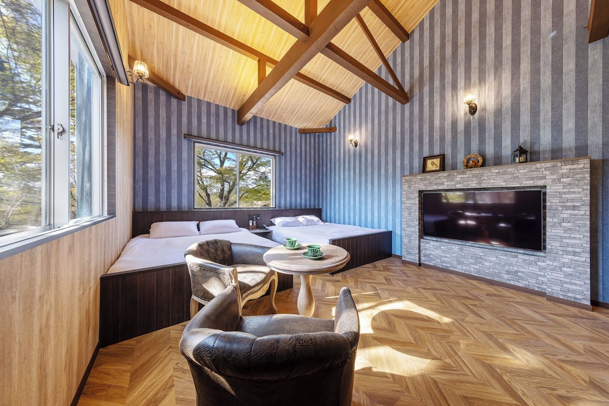 A modern room with a large bed, a fireplace, and a view of trees through a window.