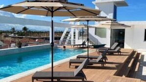A rooftop pool area with lounge chairs and umbrellas, a clear blue sky, and a modern building in the background. - Punta Cana (Punta Cana)