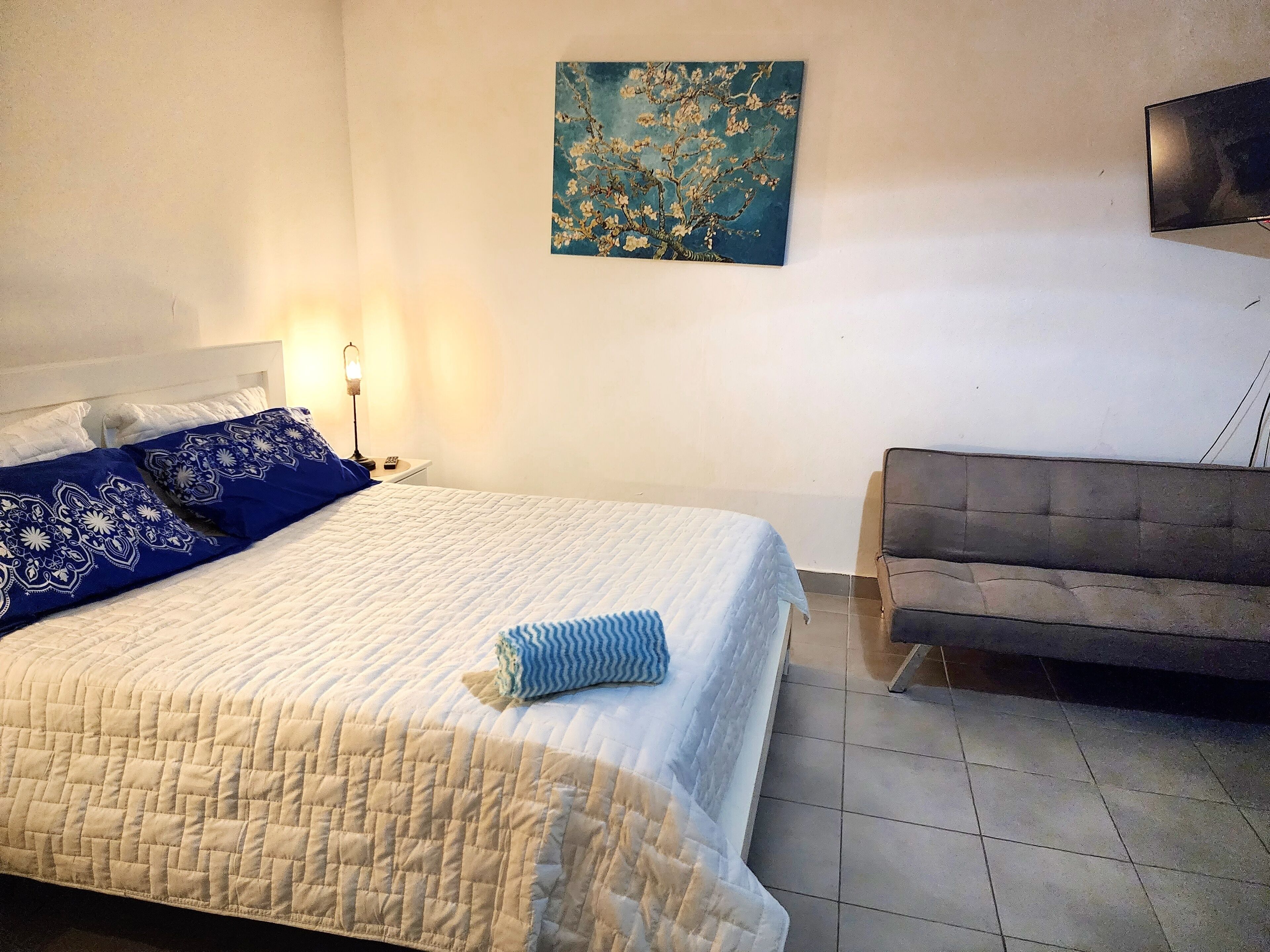 Une chambre à coucher avec un lit, une lampe de chevet, un tableau au mur et un canapé.