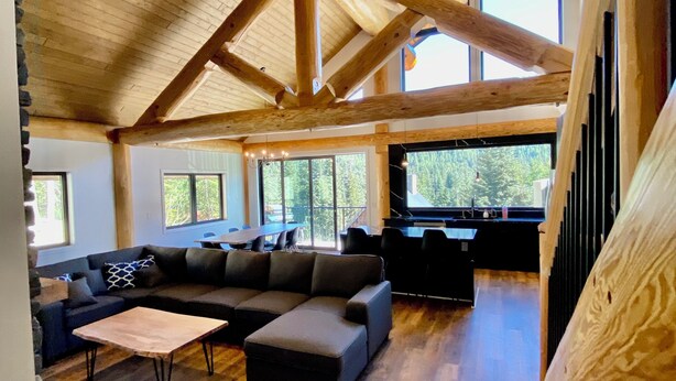 Un vaste espace de vie doté d’un haut plafond en bois, d’un canapé d’angle, d’une table basse et offrant une vue sur l’extérieur grâce à de grandes fenêtres.