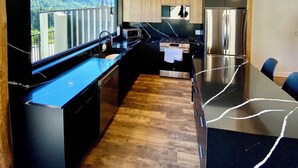 Une cuisine moderne dotée d’un grand îlot central, d’appareils électroménagers intégrés et offrant une vue sur une forêt grâce à une verrière.