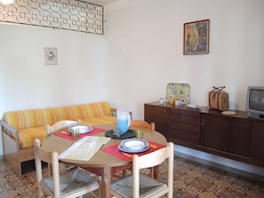 Un coin repas avec une table dressée pour deux personnes, un canapé, un meuble et un téléviseur.