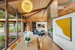 Un intérieur moderne comprenant un coin repas, des poutres en bois au plafond, de grandes fenêtres et une cheminée.