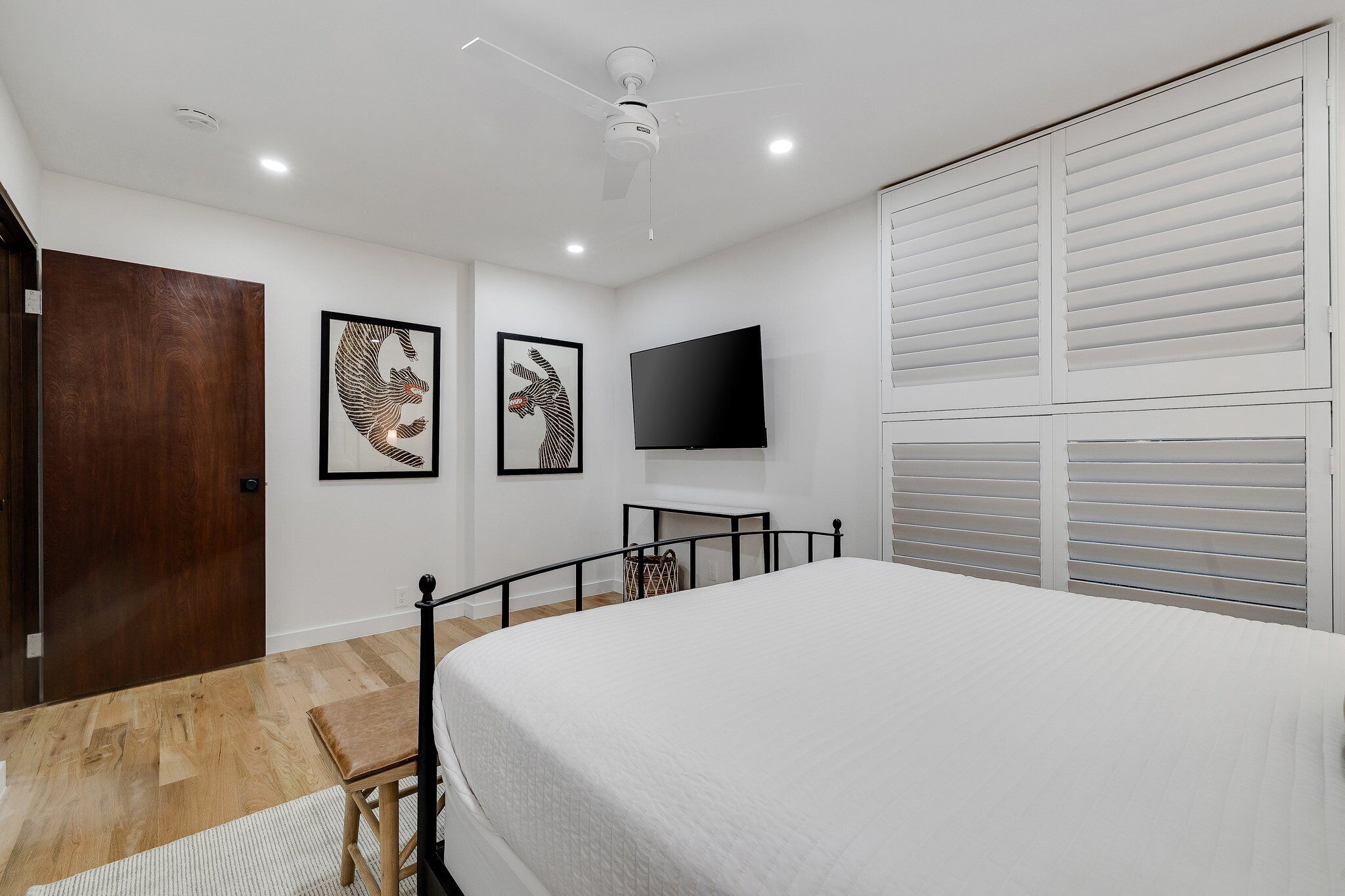 A bedroom with a bed, a ceiling fan, a TV, and a wooden door.