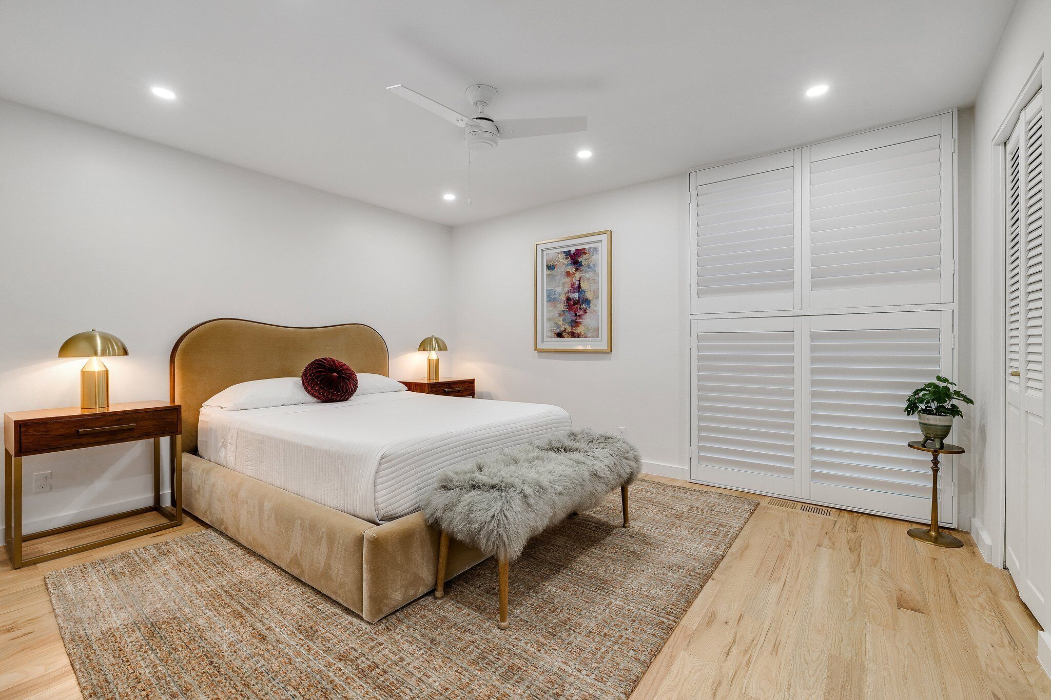 Une chambre à coucher comprenant un lit, des tables de chevet, un ventilateur de plafond, un tapis et une fenêtre avec des stores.