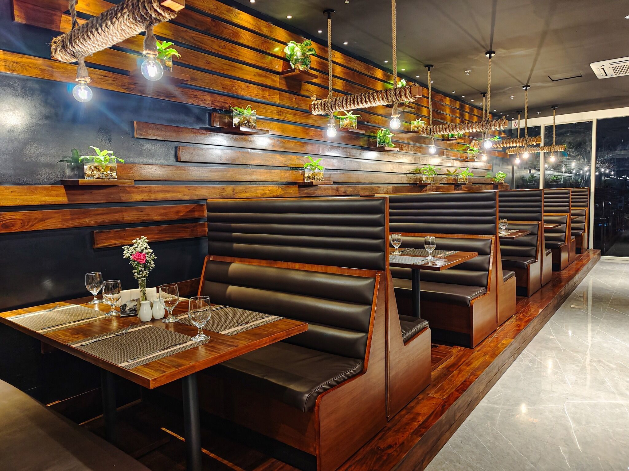 A restaurant with wooden panel walls, black leather booths, and hanging plants.