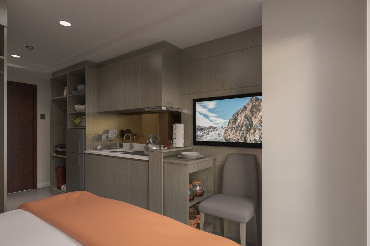 A modern bedroom with a bed, a small kitchenette, and a TV mounted on the wall.