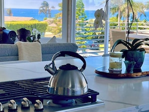 A kitchen with a kettle on a gas stove, a coffee maker, and a view of the ocean through large windows. - Perfect Zuma Beach House (Malibu)