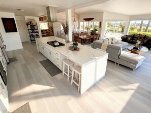 A modern kitchen with a central island, dining area with a table and chairs, and a living room with a sofa and a coffee table. - Perfect Zuma Beach House - Perfect Location & View (Malibu)