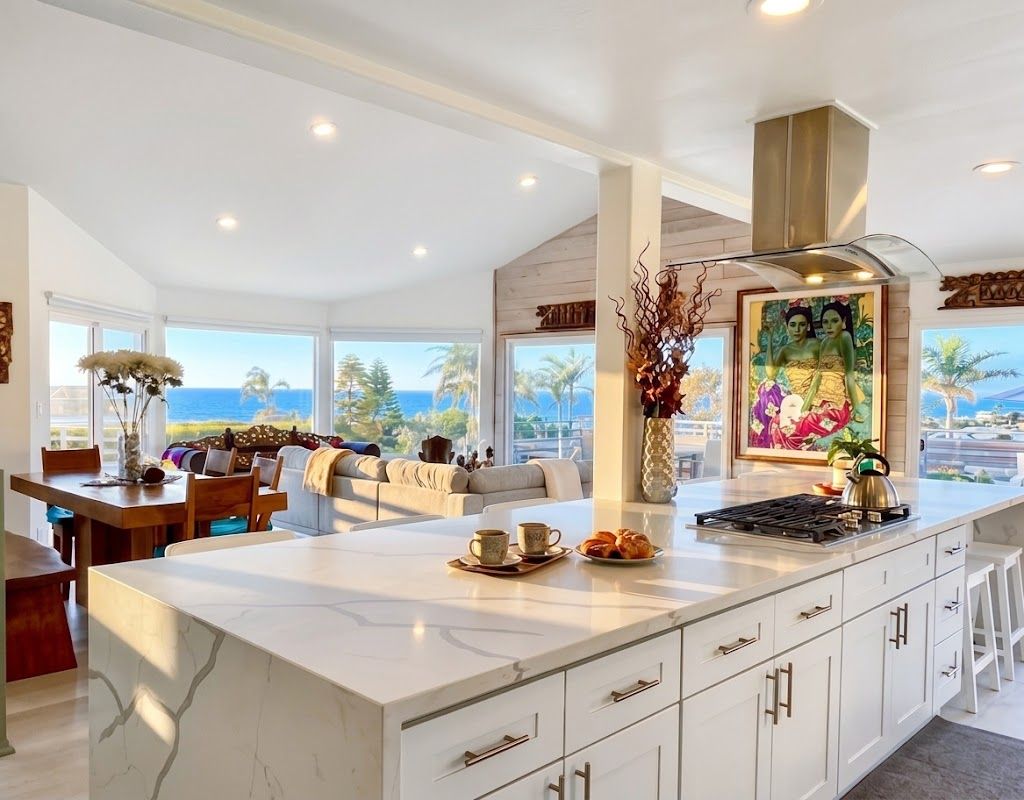 A modern kitchen with a large island, white cabinetry, and a view of the ocean.