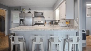 A kitchen with a large island, white bar stools, a refrigerator, microwave, stove, and cabinets. - Welcome to Catfish Cabin! (Henderson)