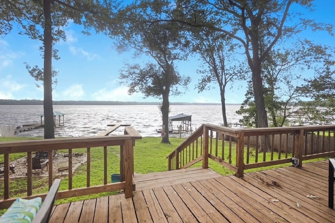 Eine Holzterrasse mit Geländer, die auf ein Gewässer mit Bäumen und einem Gazebo blickt.