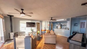 A spacious living room with a wooden floor, a sofa, a coffee table, and a television. There is a kitchen area in the background with a microwave and a stove. - Welcome to Catfish Cabin! (Henderson)