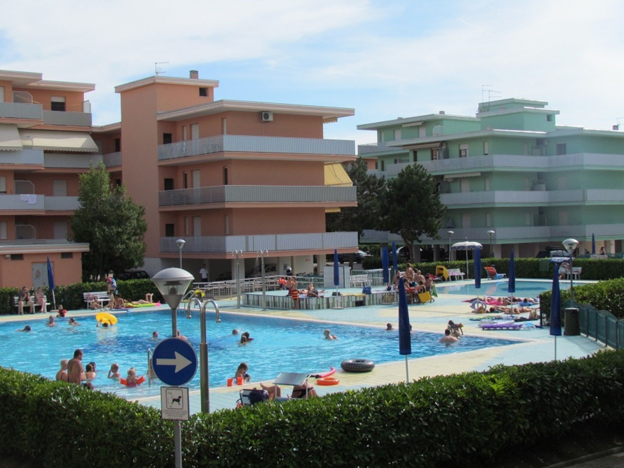 A pool area with multiple swimming pools, lounge chairs, and umbrellas. There are buildings in the background.
