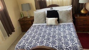 A bed with a patterned bedspread, two bedside tables with lamps, a wooden headboard, and a red rug.
