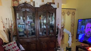 A living room with a red sofa, a wooden cabinet with glass doors, a television, and a patterned rug. - Kingmosei hide away  (Basseterre)