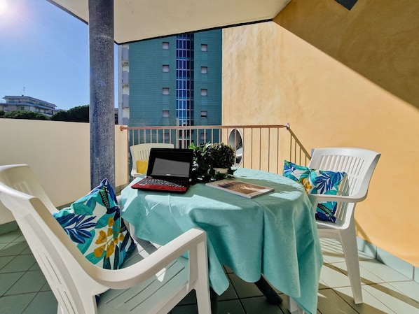 A balcony with a table, two white chairs, a laptop, and a potted plant.