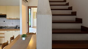 A modern kitchen with wooden cabinets, a dining table with chairs, and a staircase with wooden steps. - Holiday Apartment Nestled in a Residence With Pool (San Michele al Tagliamento)