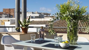 A rooftop terrace with a table set for two, featuring a potted plant, a bottle of water, and a bowl of lemons.