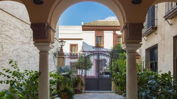 An arched corridor with a cobblestone path, leading to a gated entrance.