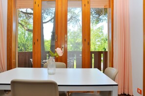 Un coin repas comprenant une table, des chaises, un vase avec des fleurs et une vue dégagée grâce à de grandes fenêtres.