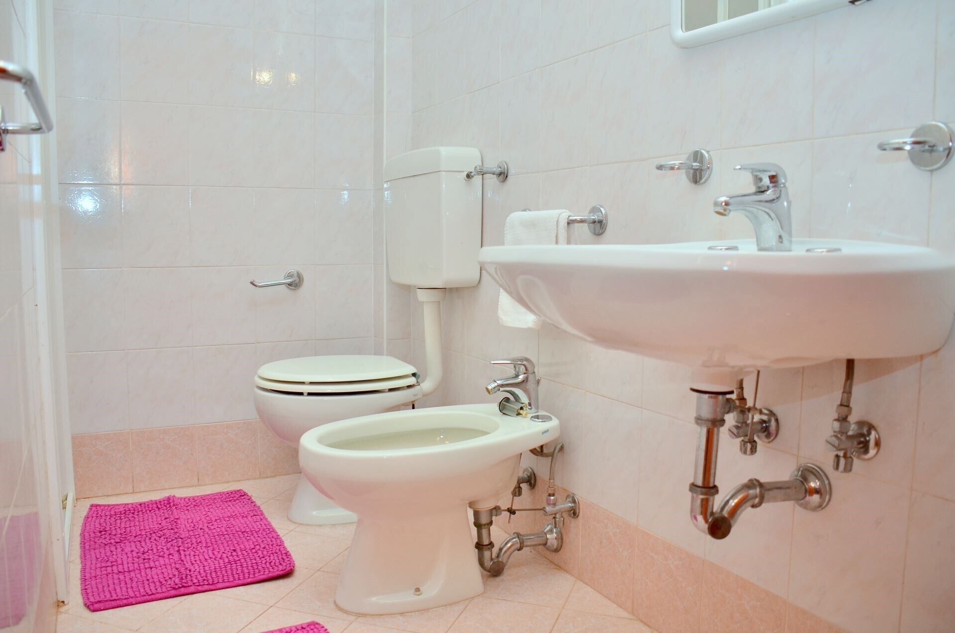 Un baño con inodoro, bidé, lavabo y una alfombra de baño rosa.