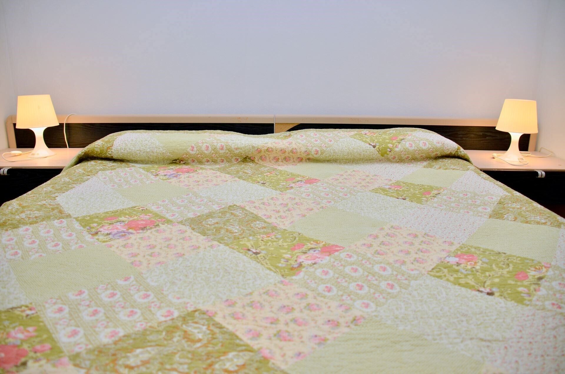 A bed with a quilt, two bedside lamps, and a wooden headboard.