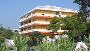 A multi-story yellow building with balconies, surrounded by greenery and parked cars. - Nice Flat With Terrace-beahost (San Michele al Tagliamento)