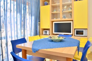 Ein Essbereich mit Tisch, Stühlen, einer blauen Tischdecke, einer Obstschale und Küchengeräten.