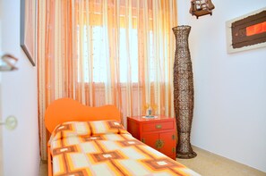 Ein Schlafzimmer mit Bett, Nachttisch, einer hohen Vase und durchsichtigen Vorhängen.