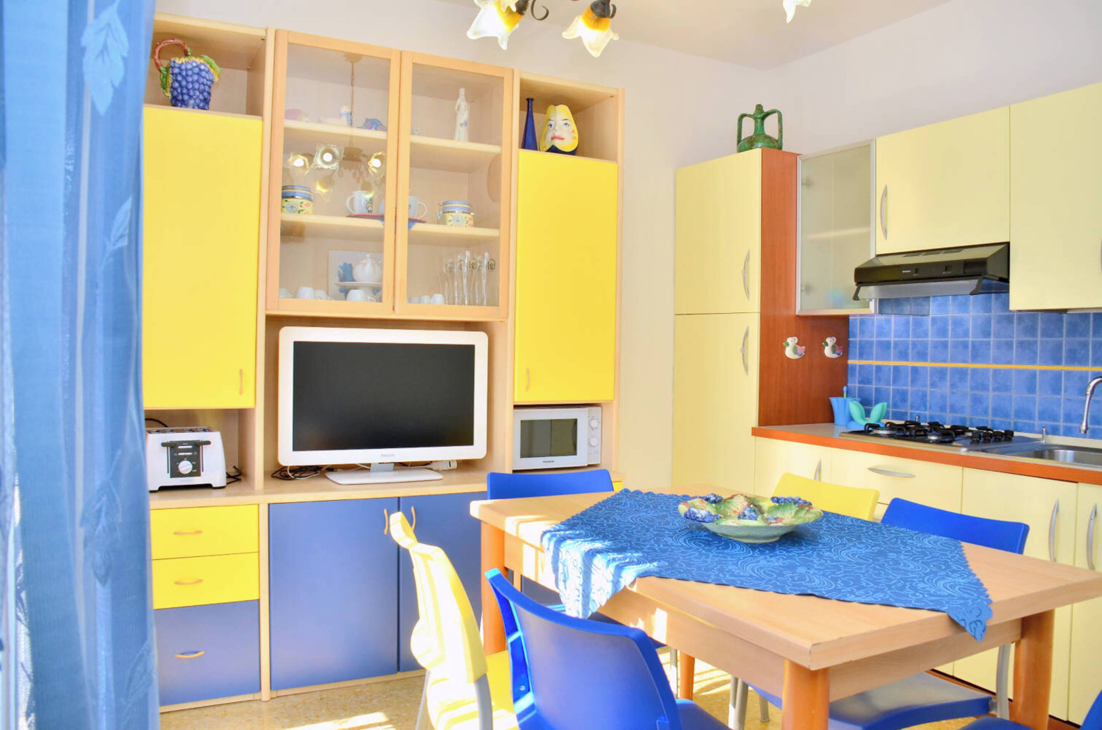 A compact kitchen with a dining area, equipped with a microwave, toaster, and a flat-screen TV.