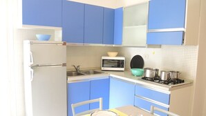 Eine kleine Küche mit blauen Schränken, einem weißen Kühlschrank, einer Mikrowelle, einem Herd und einem Esstisch mit Stühlen.