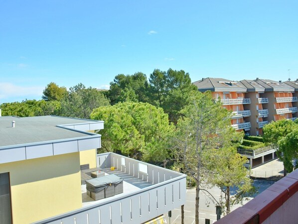 A multi-story building with balconies, surrounded by trees and a clear sky.