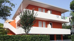 Un edificio de dos plantas con fachada roja y blanca, un balcón y un árbol en la parte delantera.