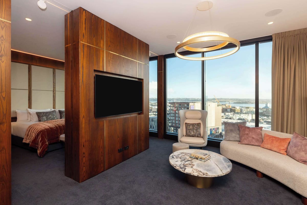 Une chambre d’hôtel moderne dotée d’une grande télévision, d’un canapé, d’un fauteuil et offrant une vue sur la ville.
