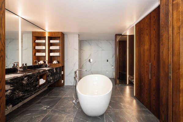 A modern bathroom with a freestanding bathtub, marble-tiled floor, wooden vanity, and a large mirror.