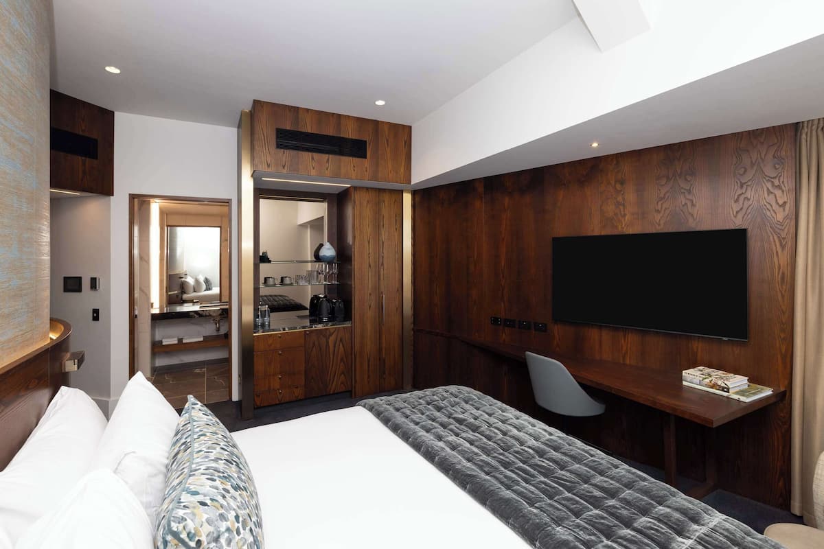 Une chambre d’hôtel moderne dotée d’un grand lit, d’un bureau avec un téléviseur à écran plat et d’un dressing.