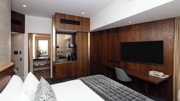A modern hotel room with a large bed, a desk with a flat-screen TV, and a walk-in closet.