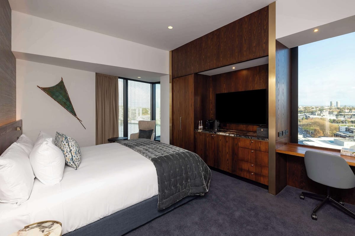 Une chambre d’hôtel moderne dotée d’un grand lit, d’un bureau avec un téléviseur à écran plat et offrant une vue sur la ville.