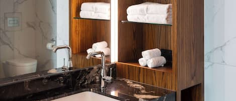 A bathroom with a marble sink, wooden shelves with towels, and a mirror.