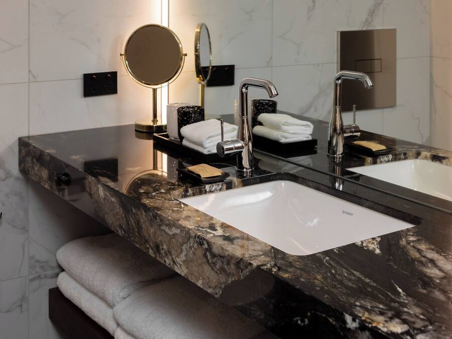 A modern bathroom with two sinks, a round mirror, and a towel rack.