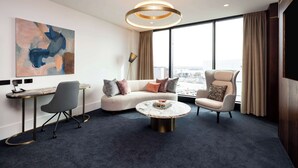A modern hotel room with a large window, a round coffee table, a sofa, a chair, and a desk with a lamp. - Horizon by SkyCity  (Auckland)