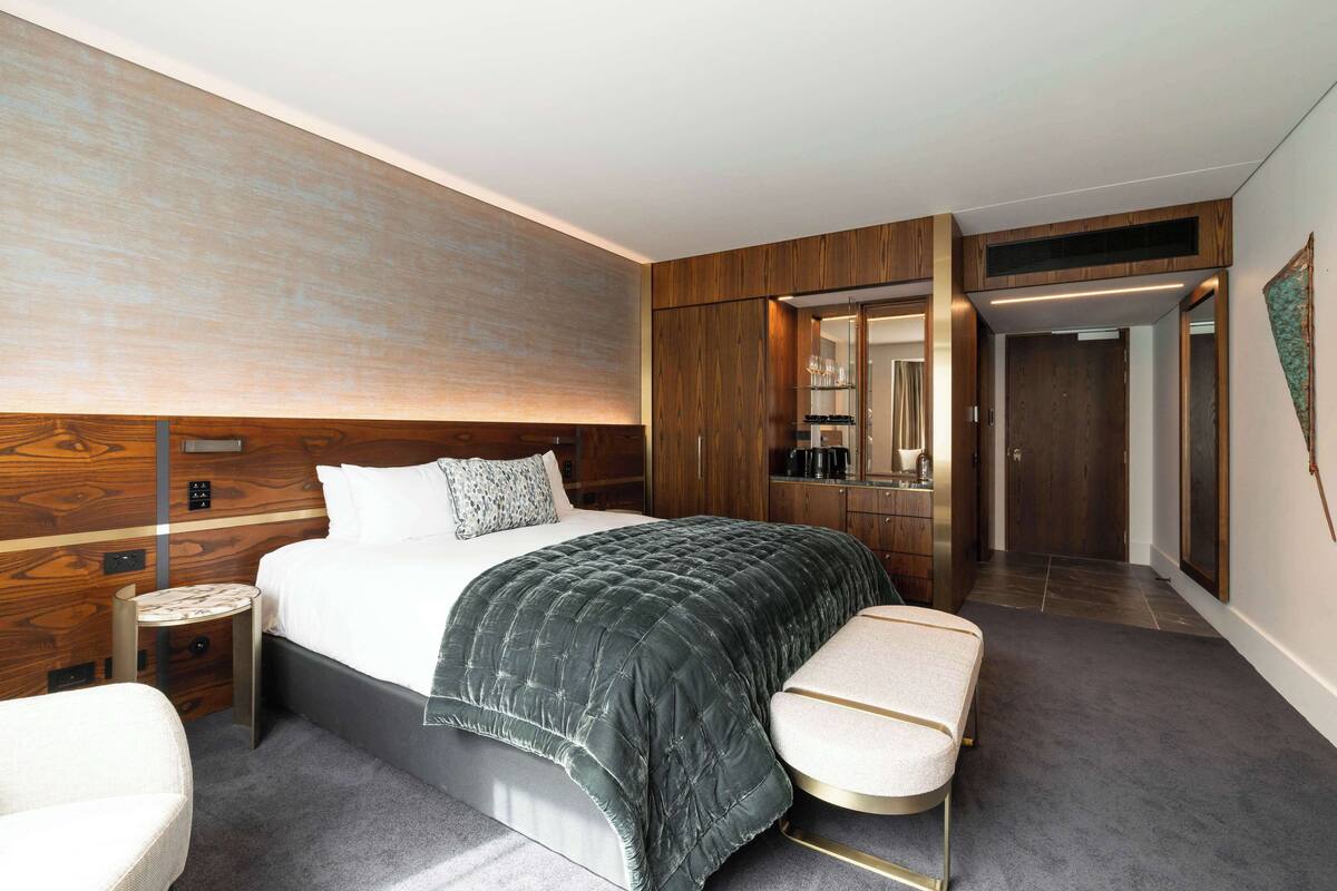Une chambre d’hôtel moderne avec un grand lit, une table de chevet, une petite table ronde, un banc et une armoire.