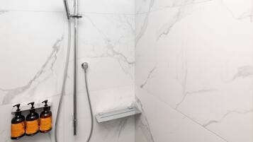 A bathroom with a shower, marble tiles, and three bottles of shampoo.