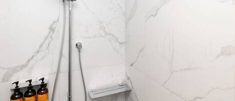 A bathroom with a shower, marble tiles, and three bottles of shampoo.