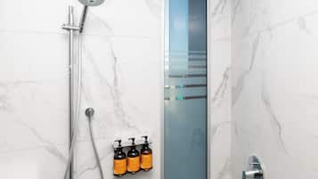 Un baño moderno con cabina de ducha de vidrio, ducha de mano y tres botellas de champú y acondicionador fijadas a la pared.