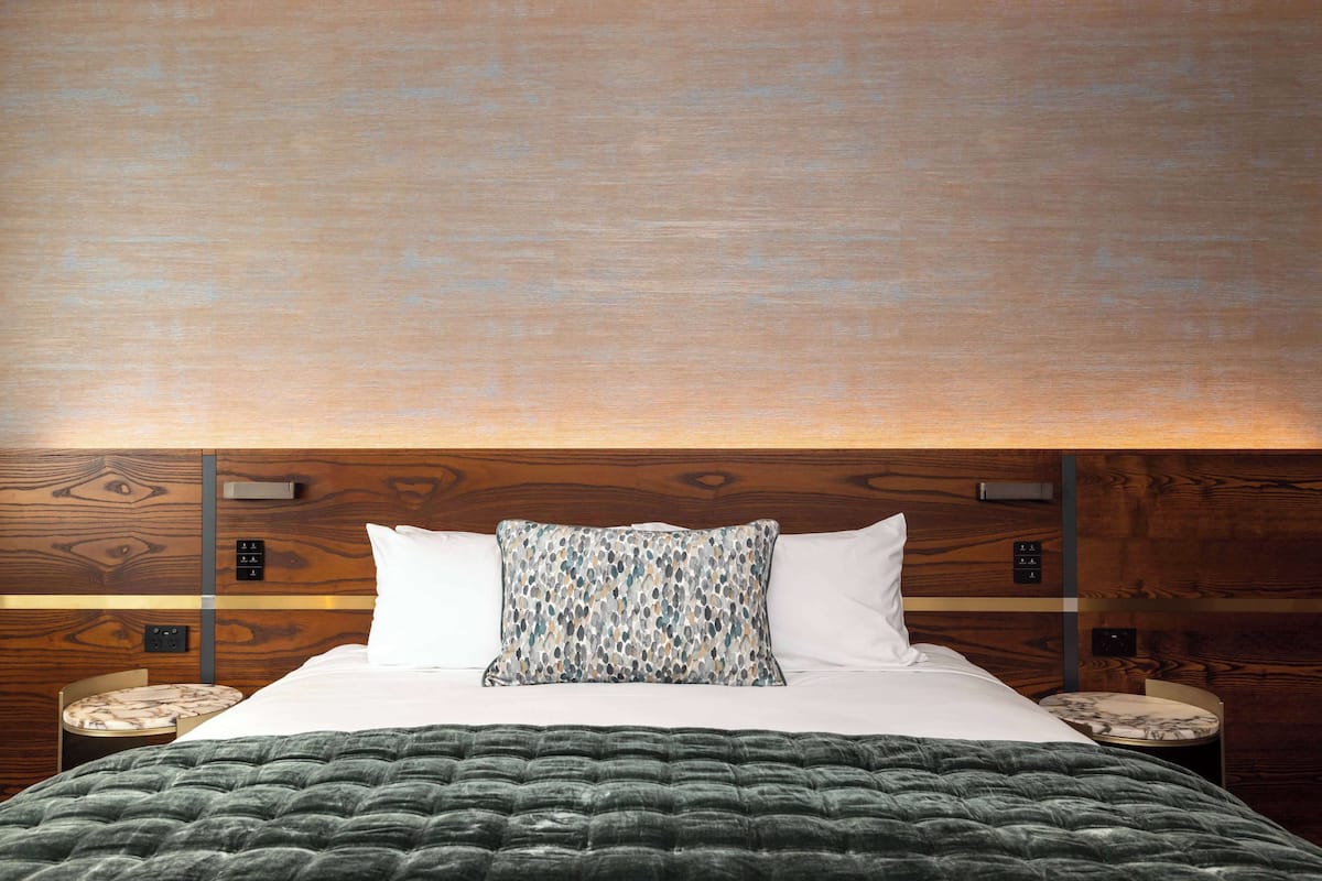 Un lit bien fait, avec un oreiller à motifs, une couverture verte et une tête de lit en bois.